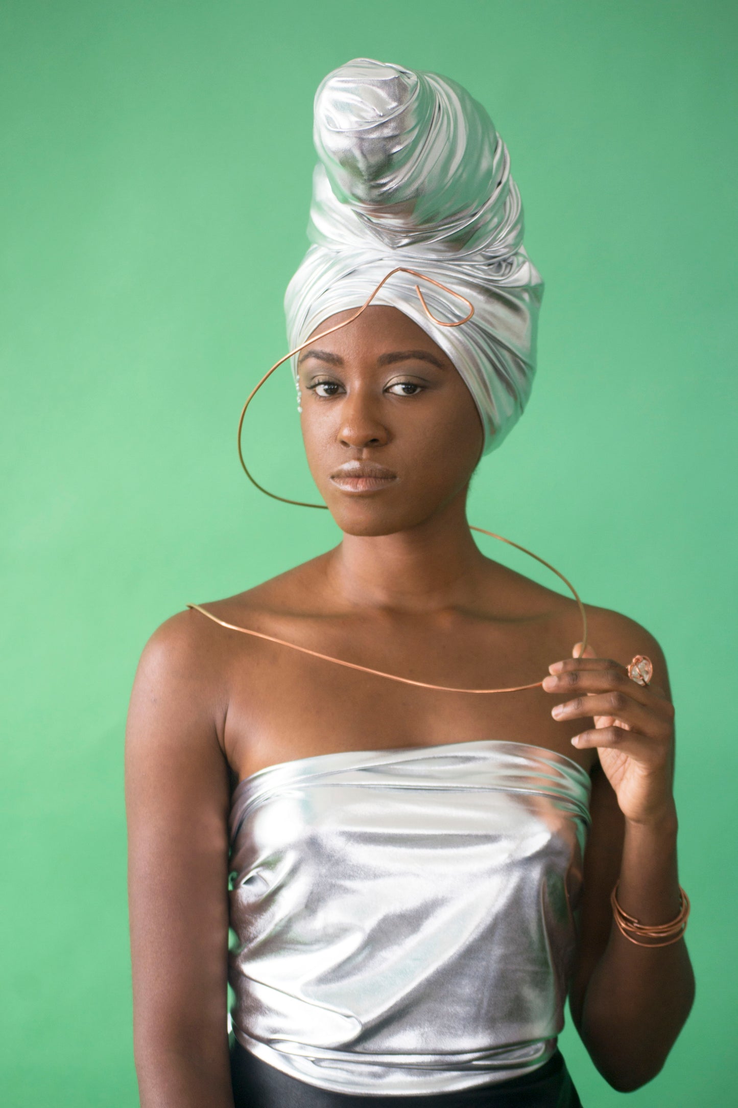 black model wearing stretchy metallic silver head wrap in cone style with copper necklace wrapped around her.