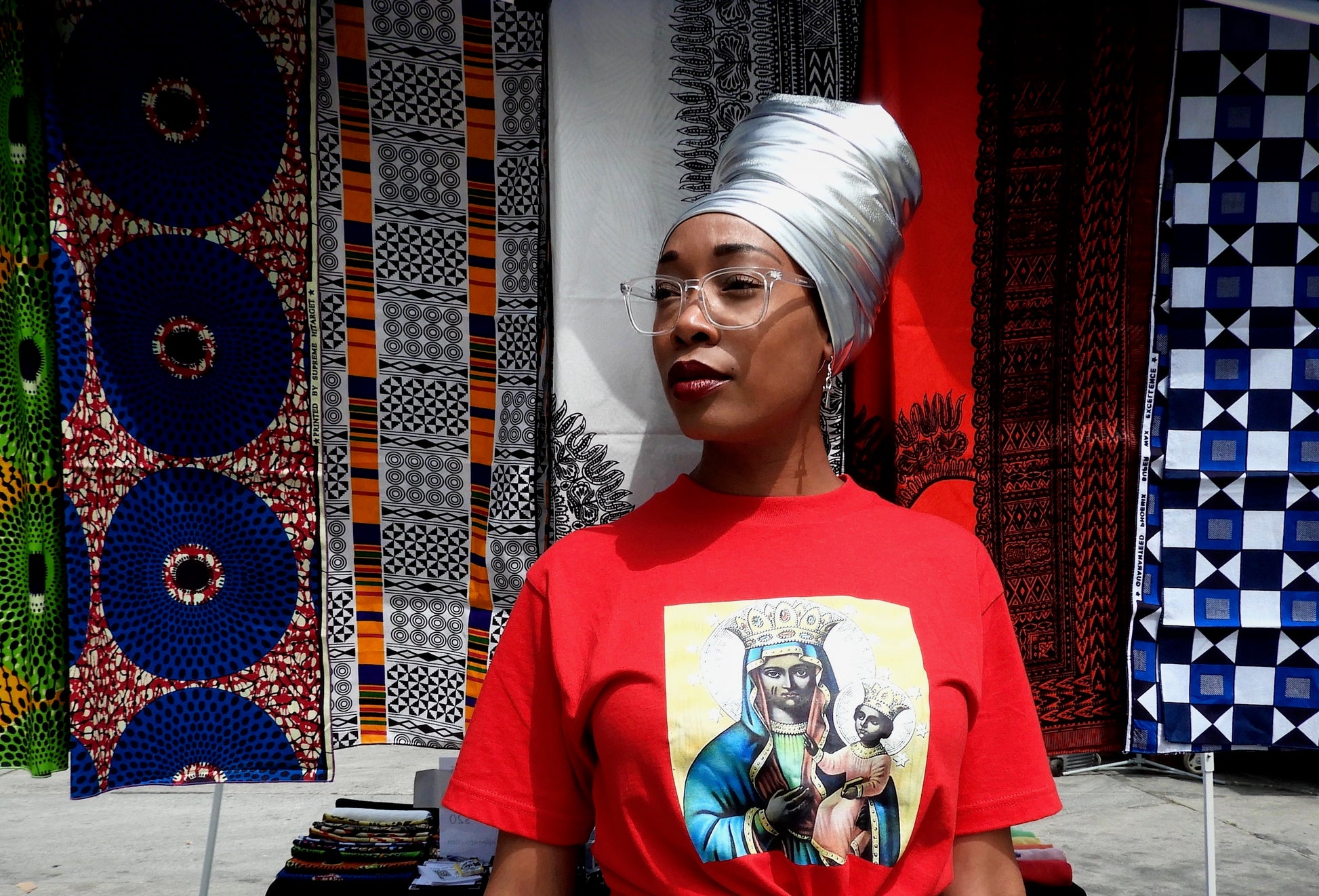 black model wearing metallic silver head wrap with printed head wraps in the background